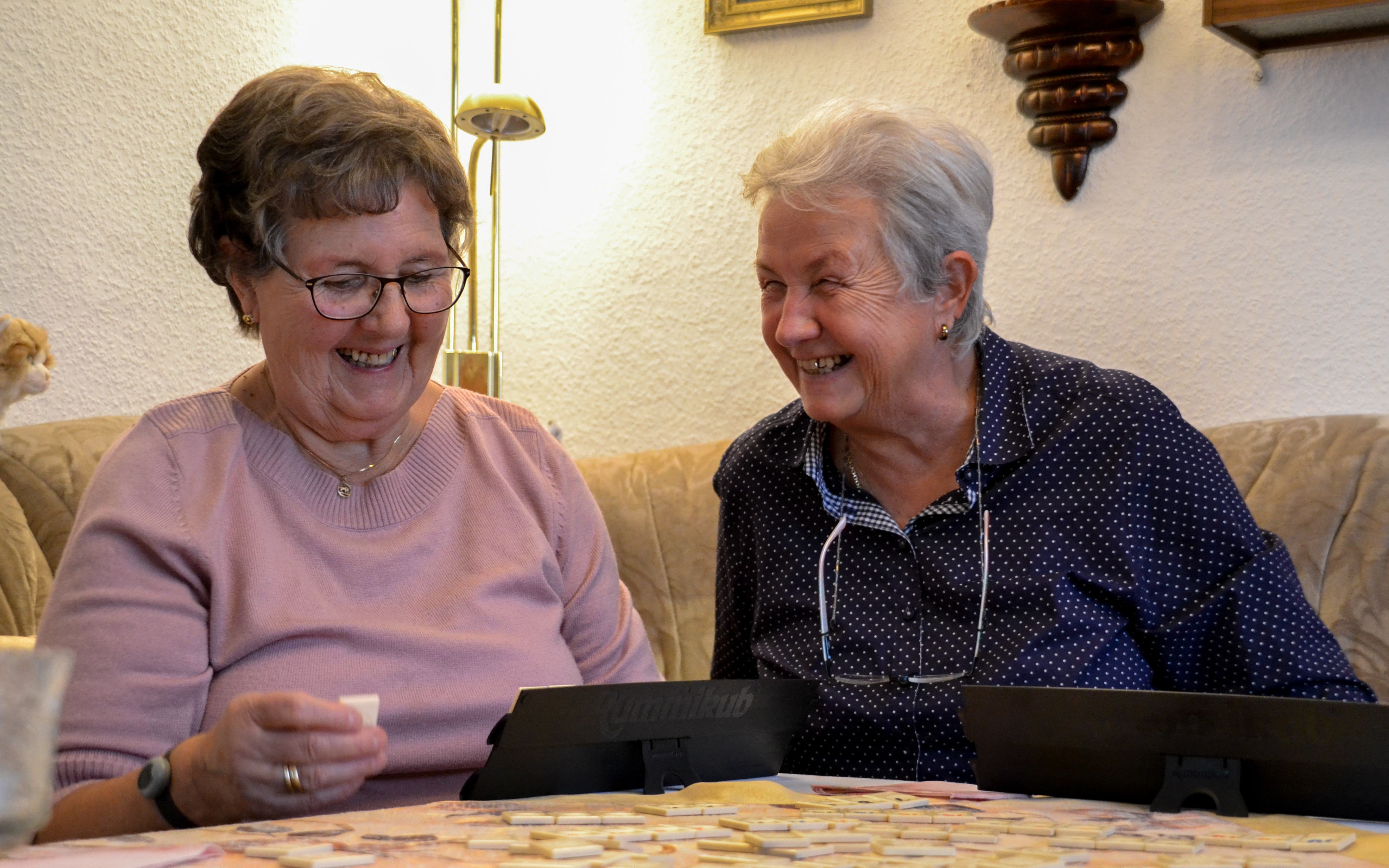 Zwei ältere Frauen sitzen an einem Tisch und spielen Rummikub.