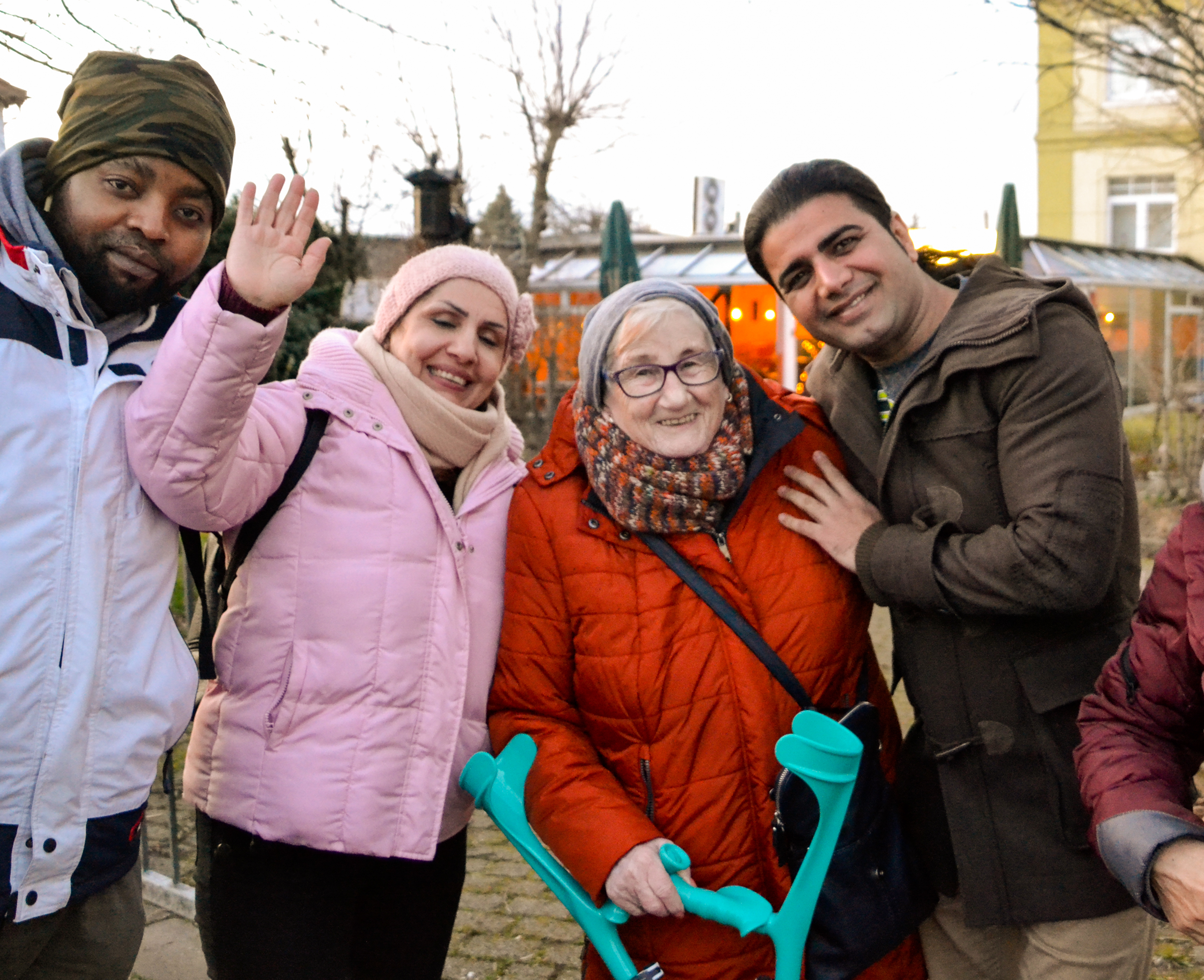 Drei ehrenamtliche mit Migrations- und Fluchterfahrung schauen gemeinsam mit einer älteren Frau in die Kamera.