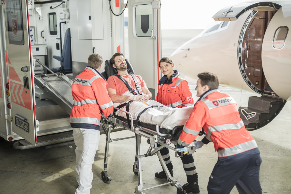 Mitarbeitende der Malteser schieben einen Mann auf einer Trage vom Flugzeug in einen Krankentransportwagen.