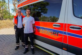 Zwei Mitarbeiter der Malteser stehen vor dem Herzenswumnsch-Krankenwagen.