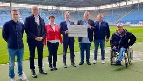 Sieben Personen übergeben im Stadion des 1. FC Magdeburg einen Spendenscheck