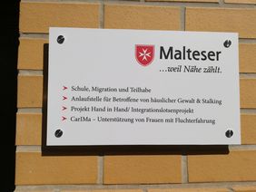 Auf einer Tafel an einer Mauer sind Projekte des Malteser Hilfsdienstes in Halle aufeglistet.