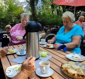 Zwei Frauen sitzen an einem Tisch im Freien, trinken Kaffee und essen Kuchen.